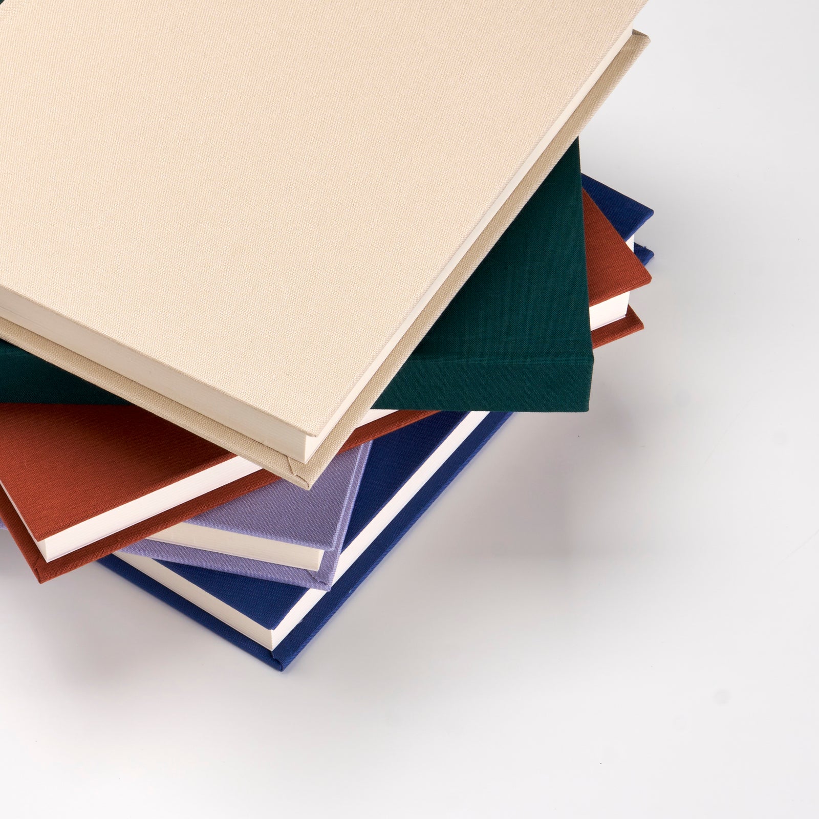 Stack of handcrafted linen photo albums in cream, terracotta, navy and forest